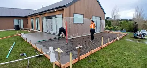Crew finishing a concrete slab beside a house